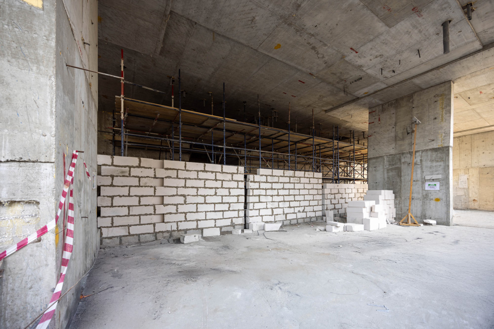Cove Edition I By Imtiaz 1 Interior construction site featuring scaffolding, unfinished walls made of blocks, and a concrete floor.